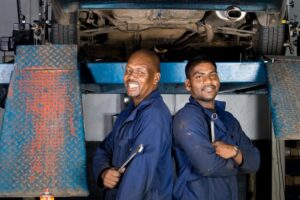 Two mechanics stand side by side in front of a car they are servicing. The extent of the TLC they offer a vehicle is determined by what is covered by either a service plan or maintenance. Which is the right option for you?
