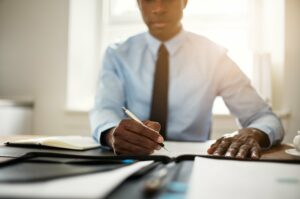 A young African businessman in a suit and tie signing an agreement over a motor warranty insurance policy.